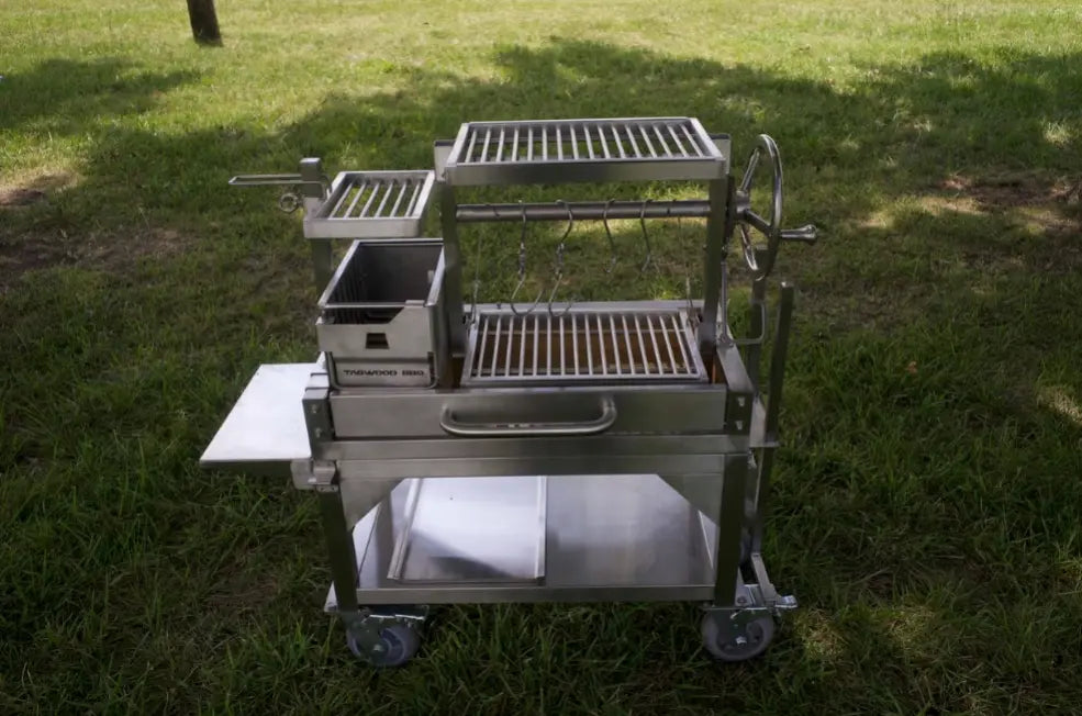 Tagwood Freestanding 'Mini' Santa Maria Style Grill featuring compact stainless steel design with four cooking zones, height-adjustable main grate, and gaucho-style brasero firebox for efficient charcoal or wood ignition.