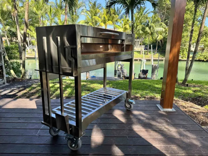 Tagwood Freestanding Santa Maria Style Grill – Stainless Steel; premium 304 stainless steel construction, featuring 705 sq. in. cooking surface, dual preset grate positions, and brasero firebox for authentic Argentine-style live-fire cooking, complete with integrated drainage system, heavy-duty casters, and included stainless steel tools and bottle opener.