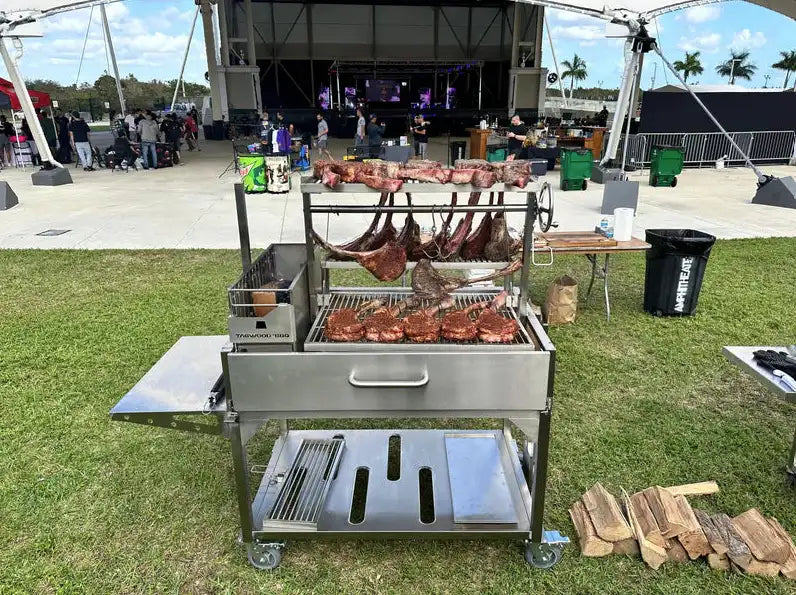Tagwood Santa Maria Style Wood Grill, stainless steel construction, features main grate with height-adjustable elevation system, secondary grate, interchangeable griddle, and S-shaped meat hooks for multi-zone cooking.