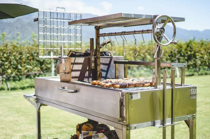 Tagwood XL Freestanding Argentine Santa Maria Style Grill: High-performance open-fire cooking station built from #304 stainless steel, featuring 2,600 sq. in. grilling area across five distinct zones, including adjustable grate and firebox with brasero for fast charcoal or wood ignition.