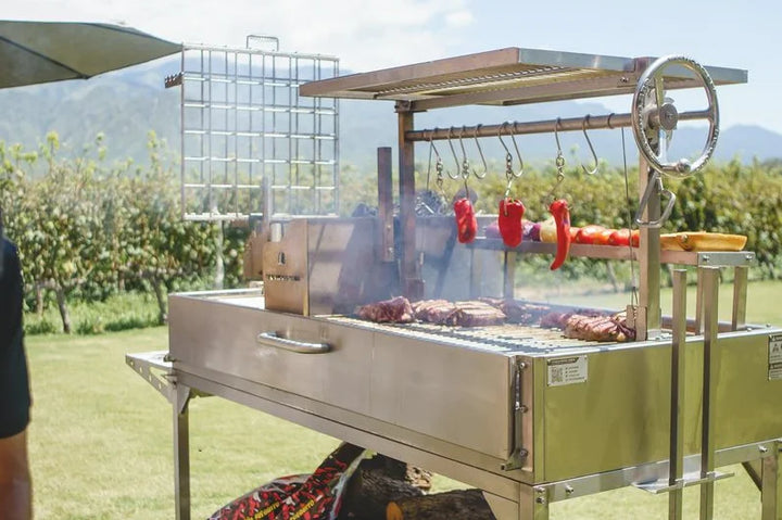 Tagwood XL Freestanding Argentine Santa Maria Style Grill featuring #304 stainless steel construction, 2,600 sq. in. grilling space across five zones, including main grate, secondary grate, clamp grill, griddle, and roofing grill.
