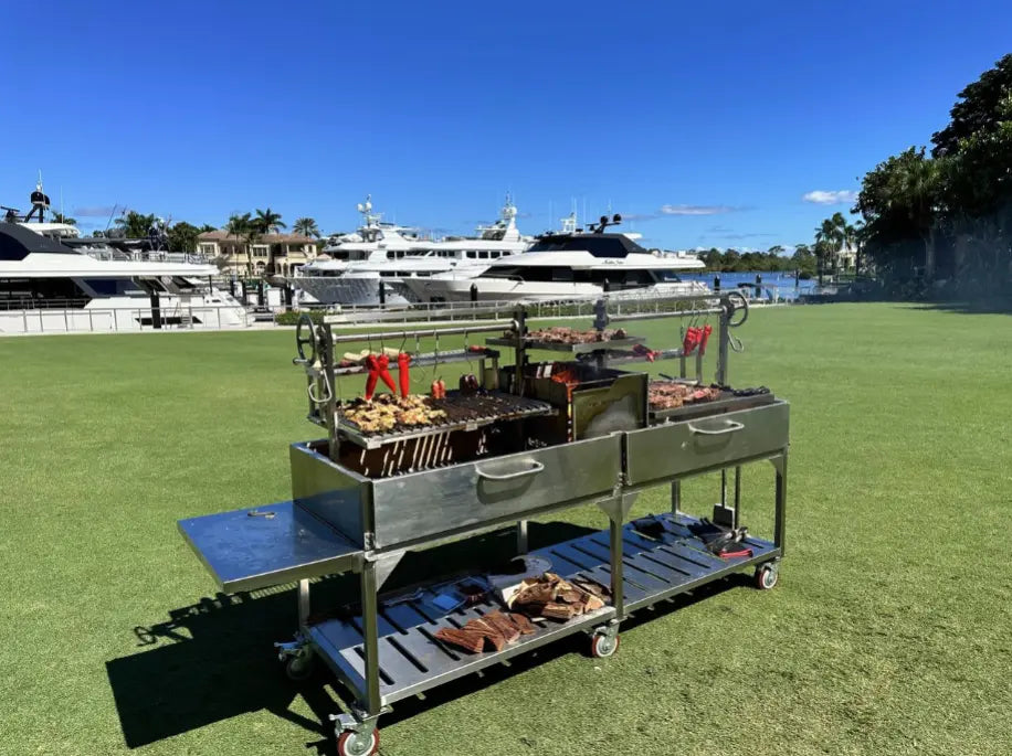 Large outdoor grill cart with food on a grassy area with yachts in the background