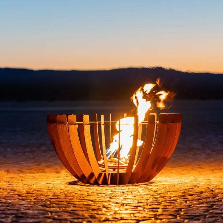 The Astro Fire Sculpture - The Outdoor Plus is a striking outdoor fire feature with curved Corten steel panels surrounding a radiant, flickering flame in a simple, bowl-shaped design, perfect for beach or patio spaces.