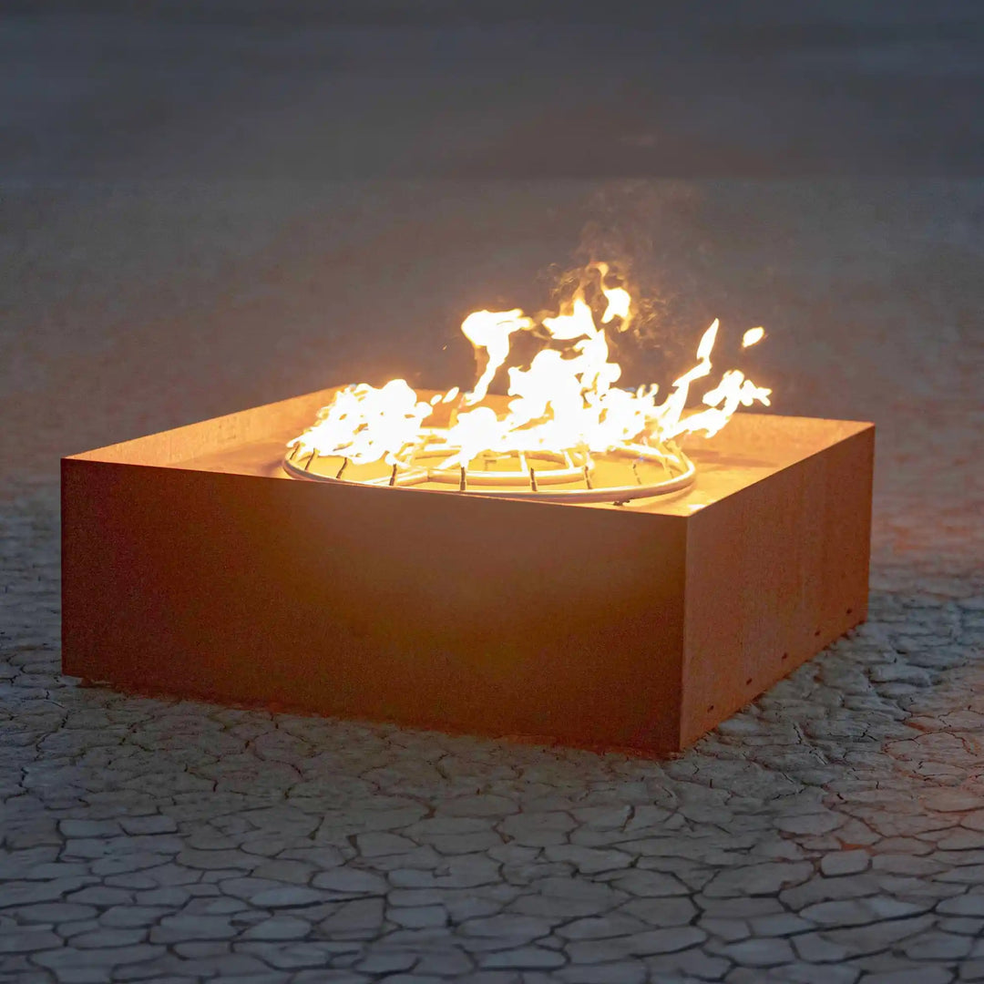 Close-up view of The Atomic Fire Sculpture - The Outdoor Plus, showcasing its modern design featuring a solid square Corten steel body with a circular burner emitting bold, clean flames from the top.