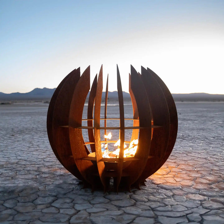 Nova Fire Sculpture by The Outdoor Plus - A modern, round fire sculpture made from curved Corten steel panels that wrap around a glowing flame, creating warmth and a sleek, open-slatted design for outdoor spaces.