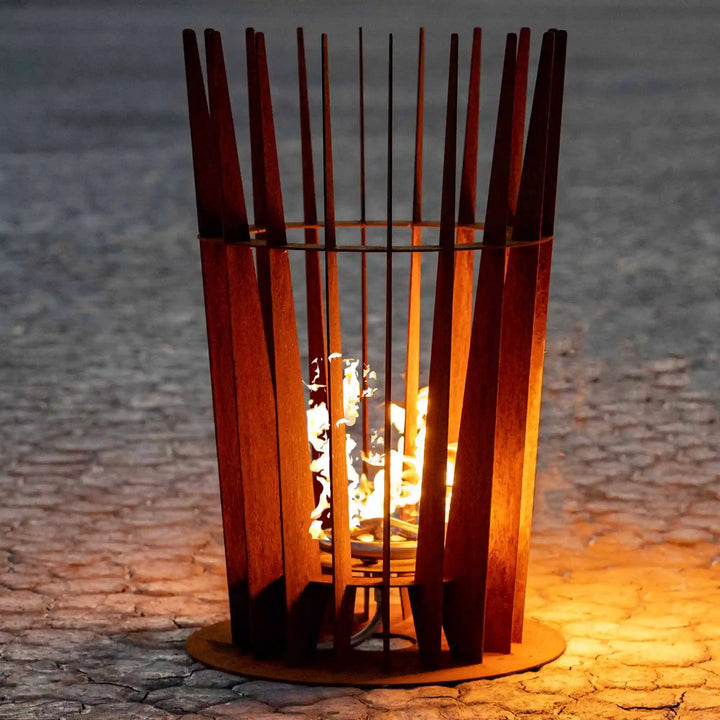 Tall Starlight Fire Sculpture - The Outdoor Plus features vertical Corten steel slats surrounding a vibrant flame that shines through gaps, emitting warmth and striking modern ambiance for outdoor spaces.