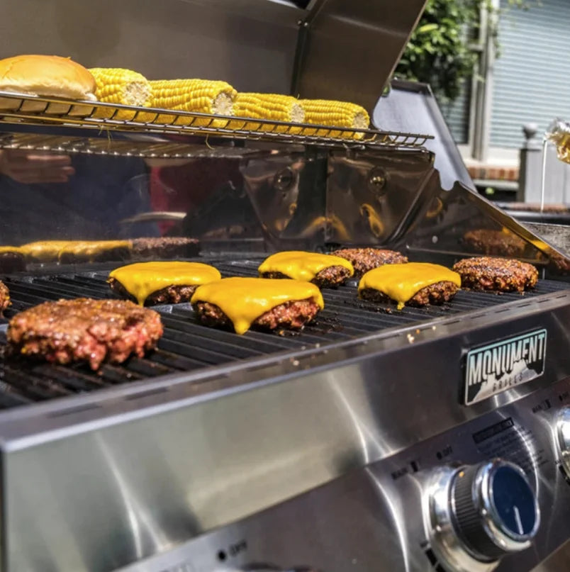 Monument Grills Classic Series 24367 stainless steel 4-burner propane gas grill with LED-lit control knobs, 723 sq in total cooking area, and side burner for versatile outdoor grilling.