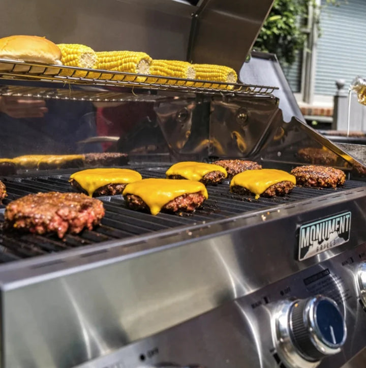 Monument Grills Classic Series 24367 stainless steel 4-burner propane gas grill with LED-lit control knobs, 723 sq in total cooking area, and side burner for versatile outdoor grilling.