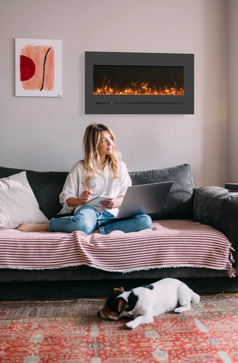 The Amantii WM-FML-STL Linear Electric Fireplace features a deep charcoal steel surround with touchpad and numerical temperature display, emitting heat from below the glass viewing area for flush mount installation.