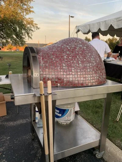 HPC Fire Forno Series Pizza Oven: Handcrafted hybrid oven with glass mosaic tile exterior, stainless steel hearth, and powder-coated black steel cart for portable and social outdoor cooking experiences.