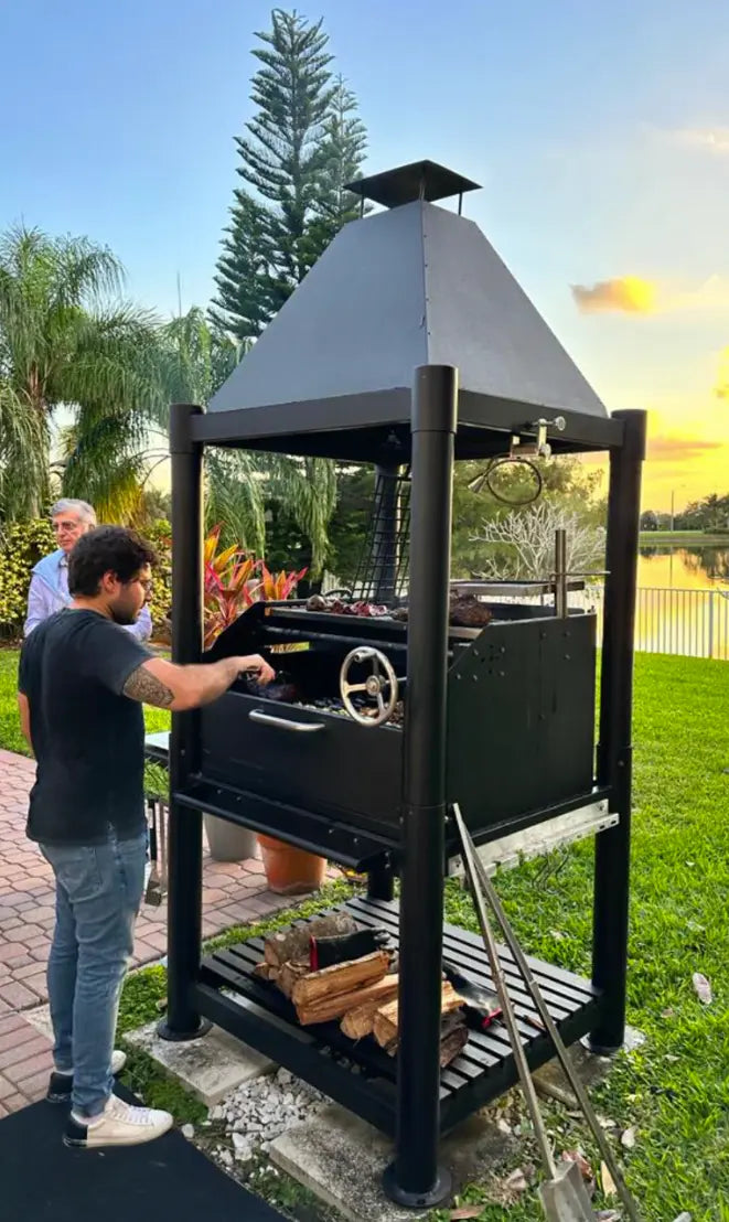 Tagwood "The Beast" Santa Maria Style Grill - Black features six distinct grilling surfaces, including adjustable dual grates, clamp grill, swivel grate, griddle, warming rack, and S-shaped meat hooks, set against a bold all-black backdrop with premium 304 stainless steel construction throughout.